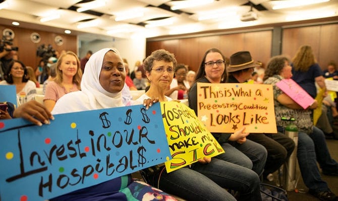 A diverse group of women hold signs to raise awareness at an indoor meeting