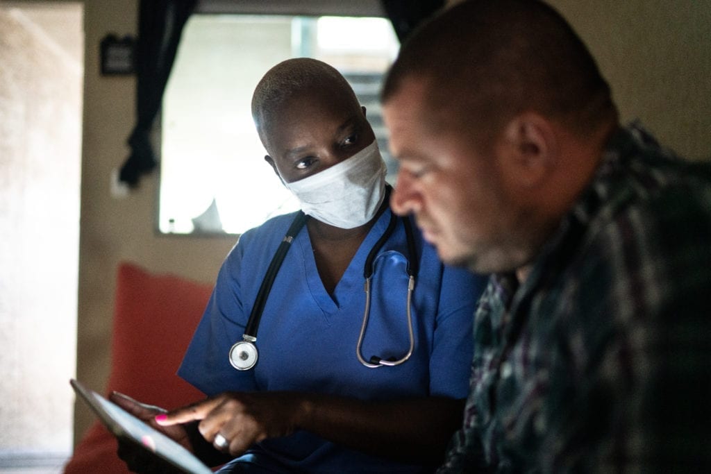Health visitor and a mid adult man during home visit - using digital tablet A nurse discusses medical plans with a patient during a home visit