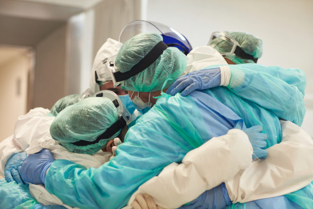 A group of medical staff members wearing protective medical gear wrap their arms around each other