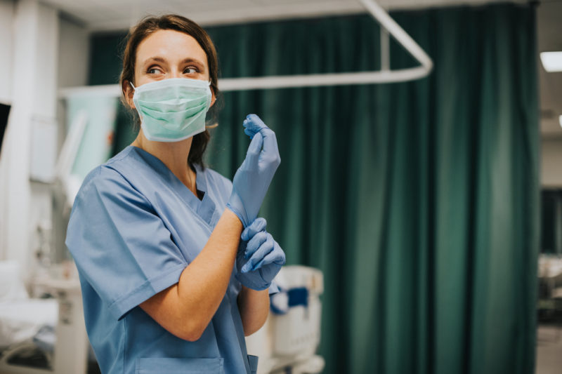 A medical staff member wearing a face covering safely prepares by putting on gloves